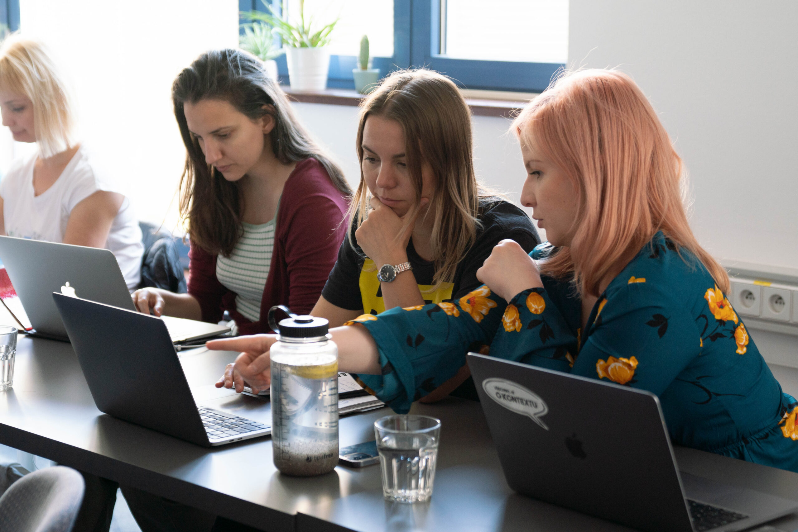A group of women collaborating at a table, each focused on their laptops, sharing ideas and working together.